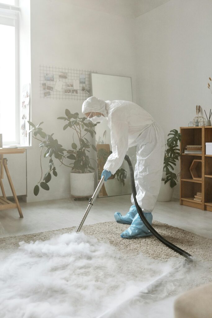 pexels-photo-4176300-4176300 A person in full protective gear disinfects a carpet in a bright indoor space.