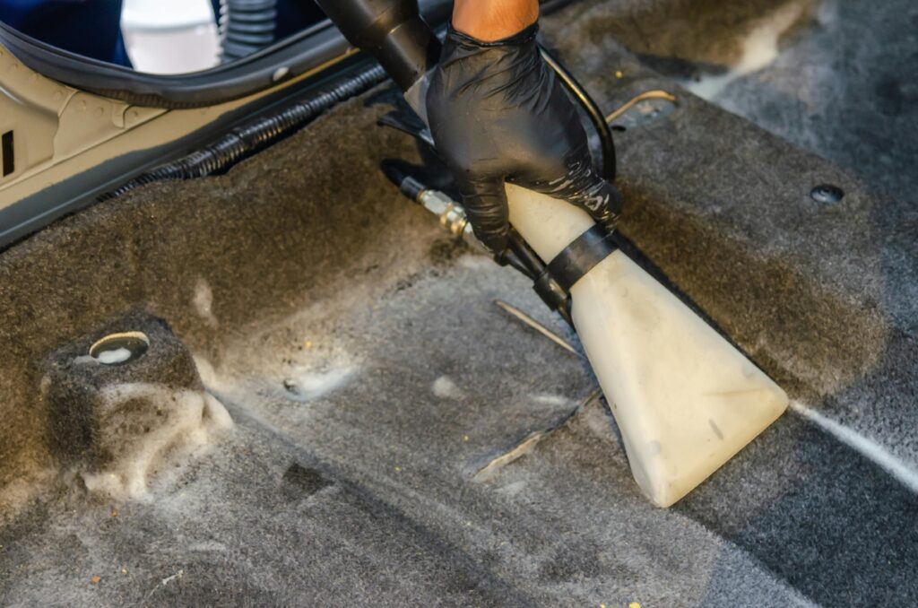 pexels-photo-5233264-5233264 A hand in a glove using a vacuum to clean a car interior carpet, removing dirt effectively.